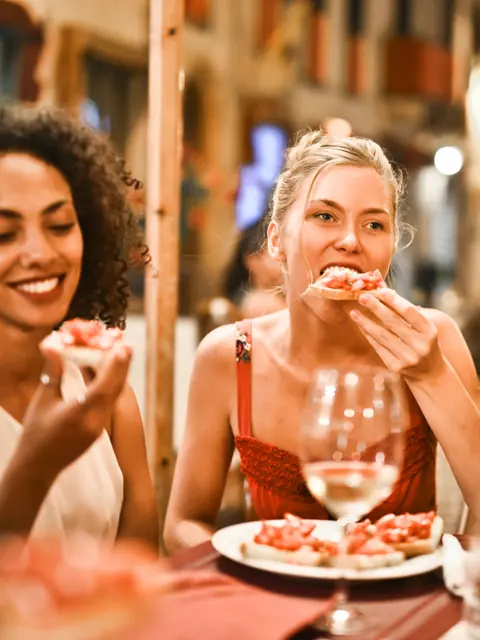 Zwei Freundinnen essen lachend in einem Bistro